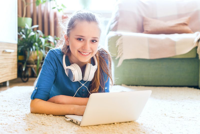 Schülerin liegt mit Laptop und Kopfhörer auf dem Boden